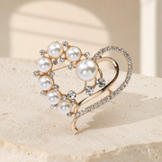 Gold-tone pearl heart brooch with clear stones on ivory limestone