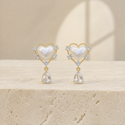 Gold-tone pearl-heart earrings with clear teardrop pendants on ivory limestone