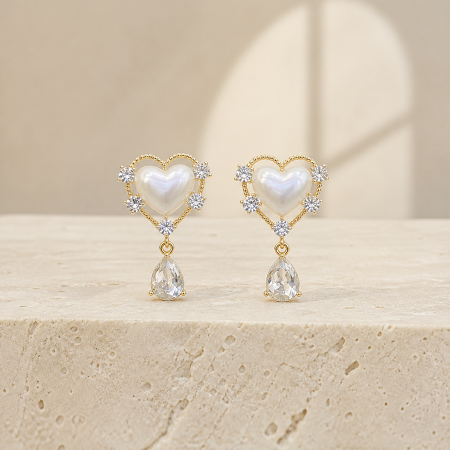 Gold-tone pearl-heart earrings with clear teardrop pendants on ivory limestone