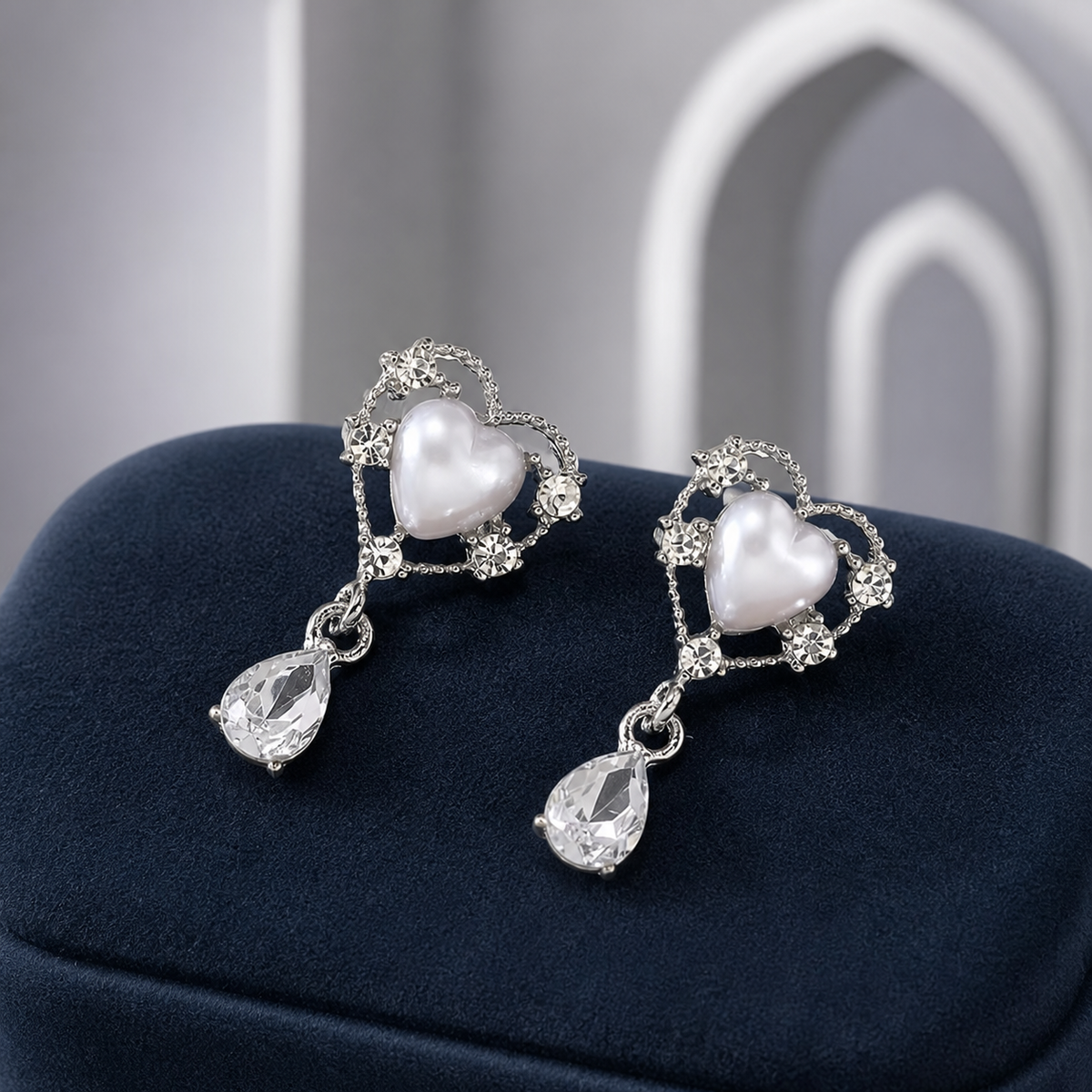 Silvery pearl-heart earrings with clear teardrop pendants on navy velvet