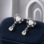 Silvery pearl-heart earrings with clear teardrop pendants on navy velvet