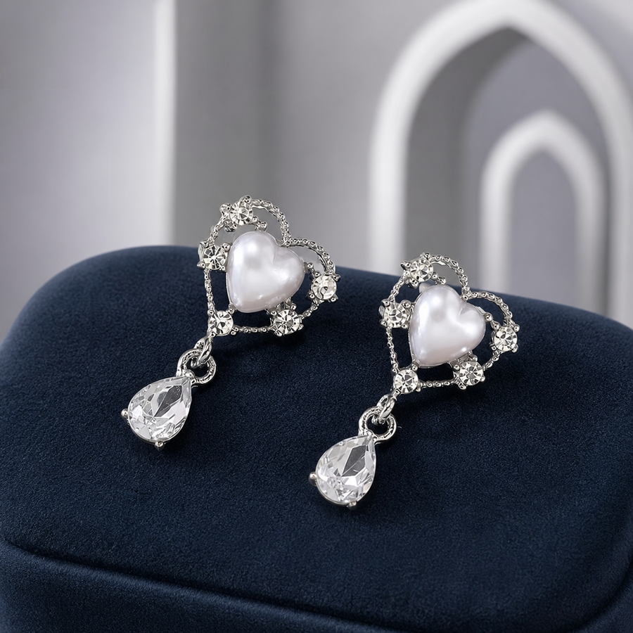Silvery pearl-heart earrings with clear teardrop pendants on navy velvet